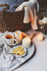 Cozy winter morning at home. Hot tea with lemon, candles, knitted sweaters in basket and modern...