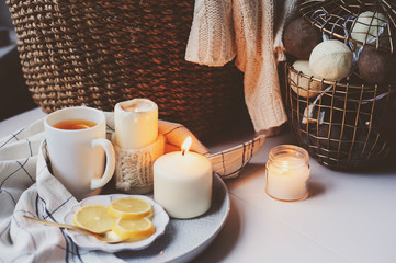 Cozy winter morning at home. Hot tea with lemon, candles, knitted sweaters in basket and modern metallic interior details. Still life composition, danish hygge concept