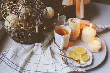 Cozy winter morning at home. Hot tea with lemon, candles, knitted sweaters in basket and modern metallic interior details. Still life composition, danish hygge concept