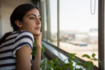 Thoughtful woman looking through window at office