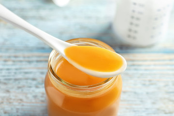 Jar and spoon with healthy baby food on wooden table