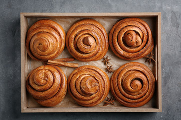 Wooden tray with sweet cinnamon rolls on table