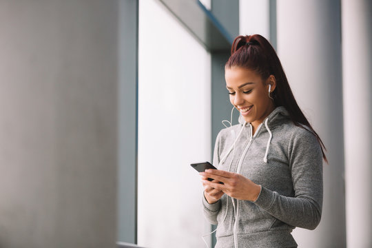 Attractive Fit Sporty Girl Typing On Her Phone And Listening To The Music Before Workout.