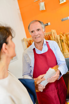 Baker serving baguette to customer