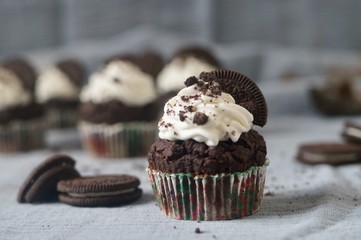 Chocolate Oreo cupcakes with whipped cream and cookie on blue-grey background.