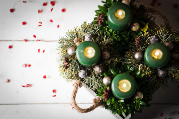 Adventsgesteck mit vier brennenden Kerzen auf weißem Holztisch
