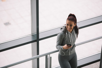 Sporty brunette typing on her phone and listening to the music before workout. High angle view.