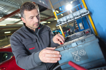 auto mechanic checks voltage level in car battery