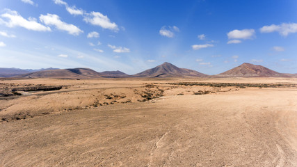 Fototapeta na wymiar Volcanic mountains panorama with rocky desert terrain , against blue, cloudy sky, Fuerteventura, Canary Islands, Spain .