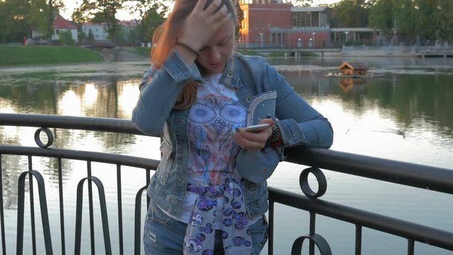 Pretty happy woman using smartphone in city park, steadicam shot