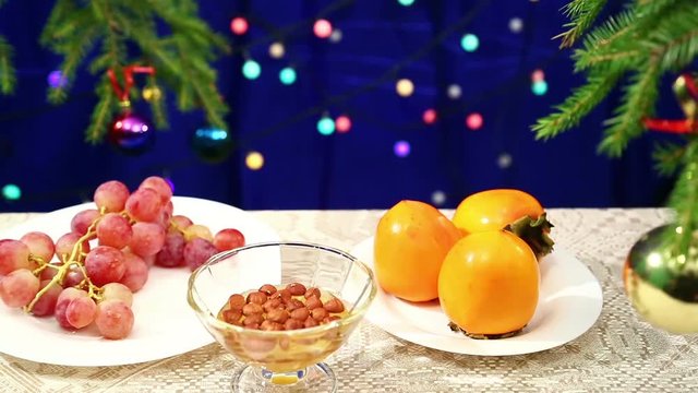 Persimmon, grapes and Nuts with honey and are on the table with a decorated Christmas tree and flashing gerunds blurred bokeh.