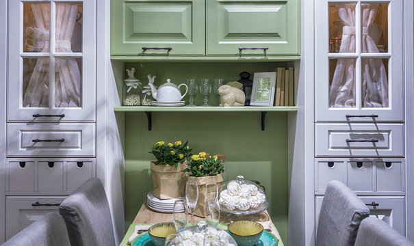 Cozy cuisine in the style of Provence. A cabinet with glass doors and a curtain as the sandglass. A wooden table, festively decorated with sweet dishes.