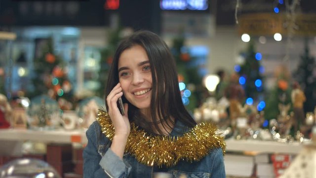 Portrait of a cheerful girl in a supermarket.
Slow motion. A young cute girl is talking on the phone.
She is in a supermarket, decorated for Christmas.