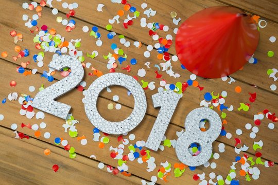 New year 2018 with party hats and confetti on wooden surface
