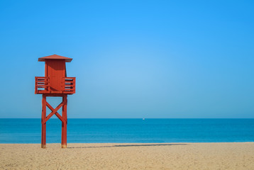 Dark red wooden lifeguard tower on the abandoned beach at Benalmadena, Malaga province, Spain. Beautiful view of the sea and sandy beach on sunny summer day with copy space.