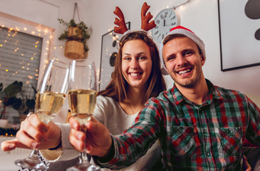 Merry Christmas and Happy New Year! Happy couple in Santa caps toasting with champagne at midnight.