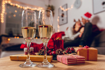 Merry Christmas and Happy New Year! Romantic couple enjoying and cuddling for Christmas at home. 
Focus on table with champagne and gifts.
