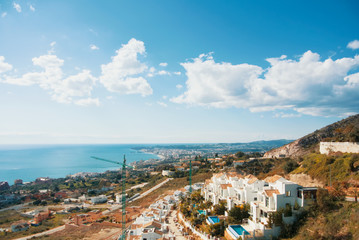 A view from the viewpoint over the hill near The Buddhist Stupa in Benalmadena town to white houses and constructional cranes, Fuengirola and Mediterranean sea at the background.