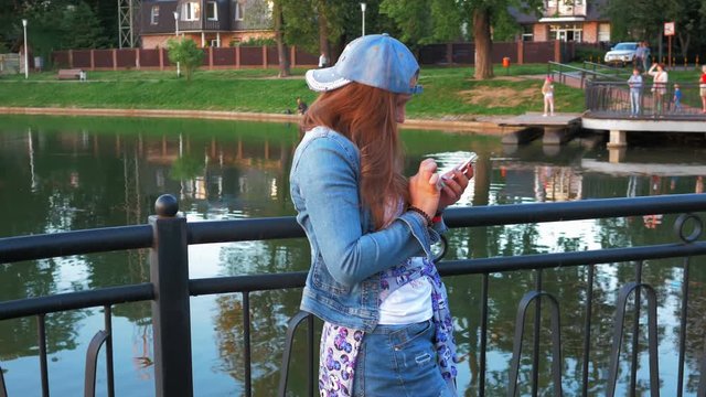 Pretty happy woman using smartphone in city park, steadicam shot