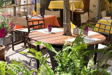 Street cafe terrace with served wooden tables and chairs decorated green plants