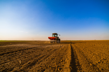Fototapeta premium Farmer fertilizing arable land with nitrogen, phosphorus, potassium fertilizer