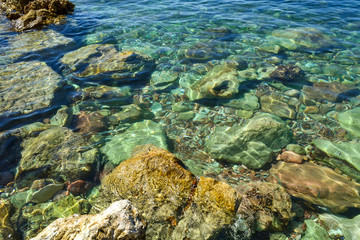 Fototapeta na wymiar Transparent sea water seethes at the shore. Large coastal colored stones in the water. Beautiful abstract background.