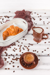 Freshly baked croissants on brown napkin, cream, to cups of coffee in ceramic dishes on white wooden background. Fresh pastries for breakfast. Delicious dessert. Closeup photography. Vertical banner