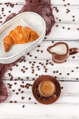 Freshly baked croissants on brown napkin, cream, to cups of coffee in ceramic dishes on white wooden background. Fresh pastries for breakfast. Delicious dessert. Closeup photography. Vertical banner