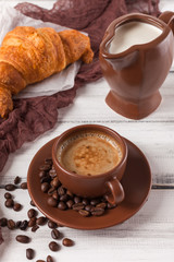 Freshly baked croissants on brown napkin, cream, to cups of coffee in ceramic dishes on white wooden background. Fresh pastries for breakfast. Delicious dessert. Closeup photography. Vertical banner