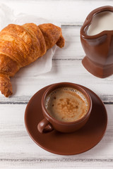 Freshly baked croissants on brown napkin, cream, to cups of coffee in ceramic dishes on white wooden background. Fresh pastries for breakfast. Delicious dessert. Closeup photography. Vertical banner