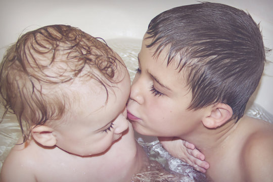Big brother plays with little brother in the bathroom and kisses him on the cheek