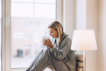 Beautiful white stylish woman in cozy scandinavian interrior sits at home near the big window, portrait of the beautiful girl, fashion portraits, woman with style © thekotlyar