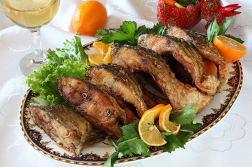 Fried fish-a carp on a plate decorated with greens with lemon and white wine.