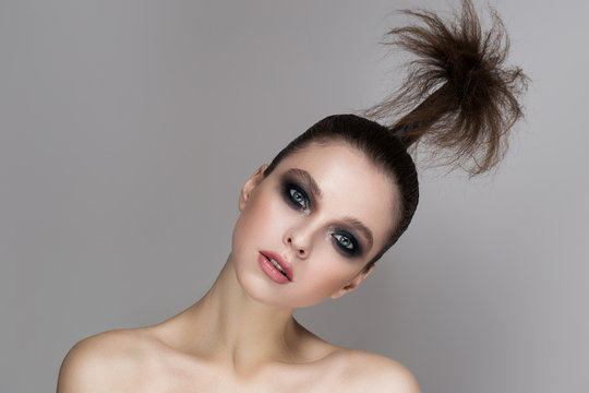 A young girl with bright makeup and radiant skin. Creative hairstyle on the head. On a gray background.