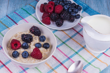 Oatmeal porridge with berries and milk on a rustic wooden background - a healthy organic breakfast
