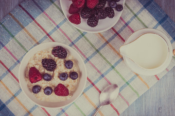 Oatmeal porridge with berries and milk on a rustic wooden background - a healthy organic breakfast
