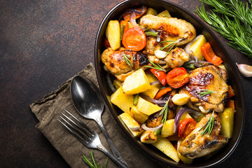 Chicken baked with vegetables. Top view with copy space on dark rusty table.