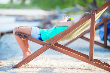 Adorable little girl relaxing in colorful wooden chair at beach during summer vacation