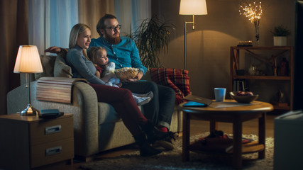 Long Shot of a Father, Mother and Little Girl Watching TV. They Sit on a Sofa in Their Cozy Living...