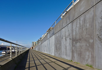 Esplanade along the Europa harbor in Bremen, Germany with metal railing, gray concrete wall, moored sailing yachts and a blue sky