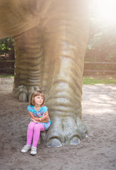 Cute little girl under huge diplodocus dinosaur