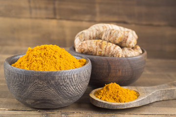 Turmeric powder and fresh turmeric on wooden background