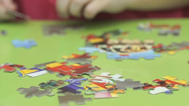 Close-up of unidentified little child collect picture from puzzles sitting at desk in kindergarten