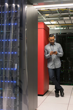 Server room technician leans on bank of servers looking down at
