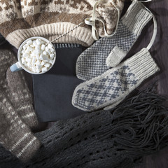 the Woolen mittens, scarf and sweater with a black notepad for notes lie on the table. Copy space.