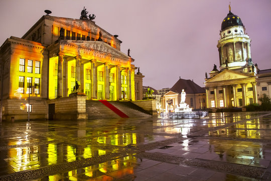 A view of famous Gendarmenmarkt square with illuminated Concert Hall and French Cathedral reflecting on wet floor after rain in twilight during sunset in Berlin city center