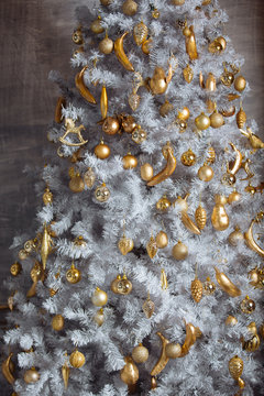 Golden christmas toys hanging on white artificial christmas tree