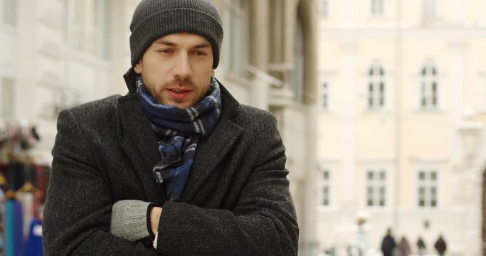 Portrait shot of the caucasian good looking man in casual style is freezing on the cold winter day while standing in the center city. Outside
