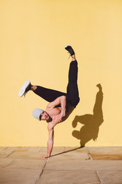 Man breakdancing in front of a yellow wall.