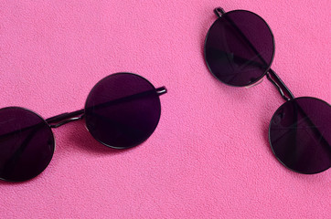 Two stylish black sunglasses with round glasses lies on a blanket made of soft and fluffy light...